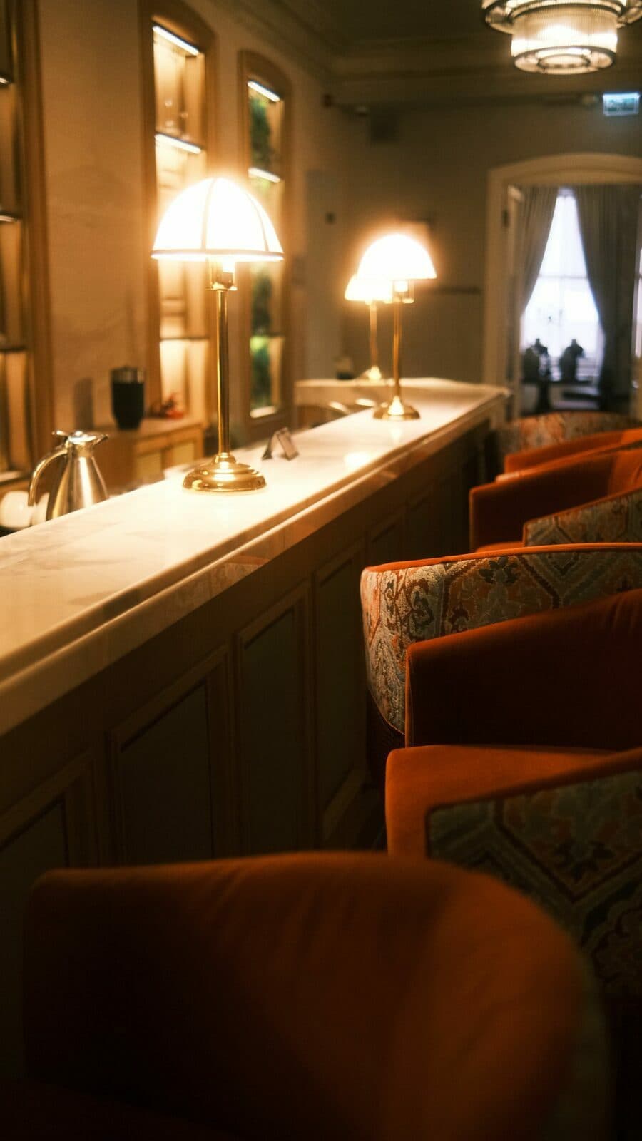 A hotel bar in warm lamplight, velvet chairs waiting